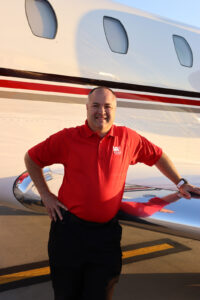 Jeremy Hill smiling and leaning on the wing of a white, red, and gray striped plane